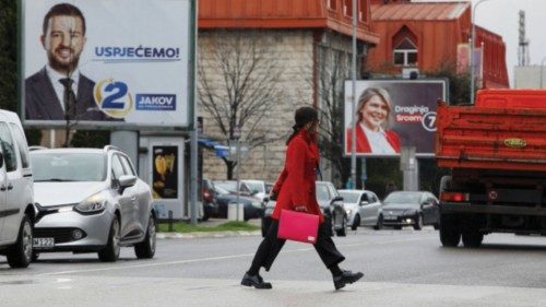 A pedestrian crosses street in front of pre-election billboards of candidates Jakov Milatovic and ...