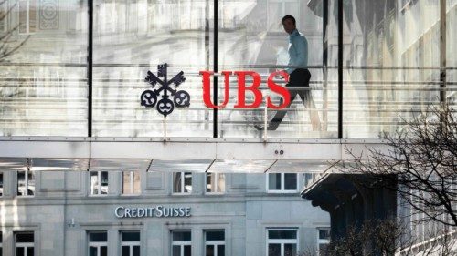 A employee is seen in silhouette next to a sign of Swiss giant banking UBS and a sign of Credit ...