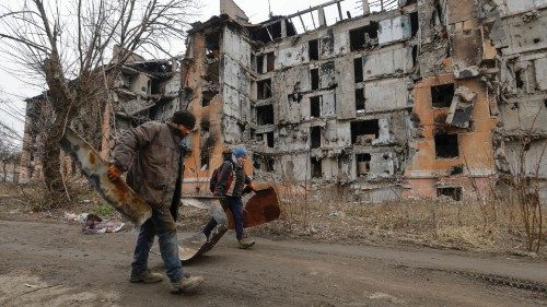 Local residents walk past a multi-storey apartment block, which was destroyed in the course of ...