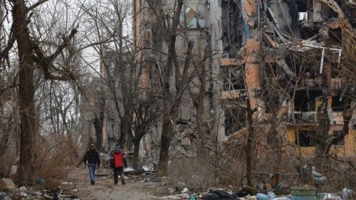Men walk near multi-storey apartment blocks, which were destroyed in the course of Russia-Ukraine ...