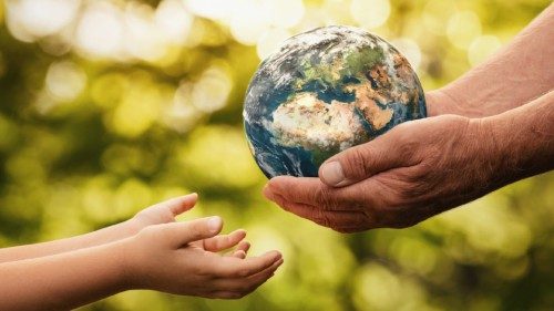 Close up of senior hands giving small planet earth to a child over defocused green background with ...