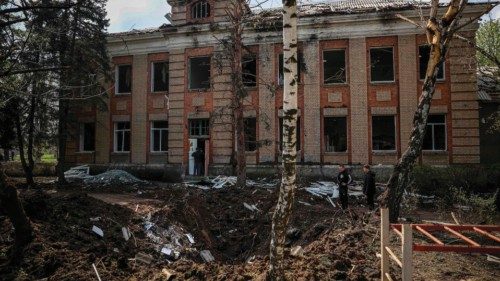 Teenagers stand next a crater left by a missile attack in front of a damaged school building in ...
