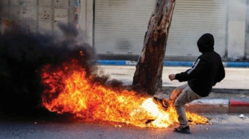 A Palestinian kicks a burning object during clashes between Palestinians and Israeli soldiers ...