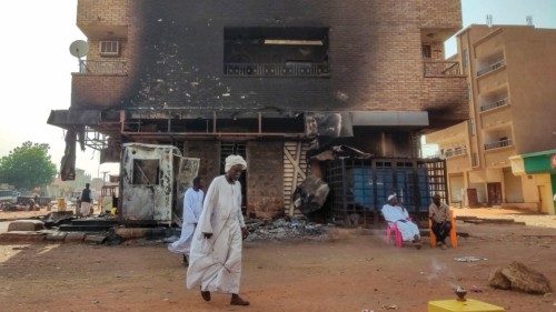 Men walk past others sitting outside a burn-down bank branch in southern Khartoum on May 24, 2023. ...