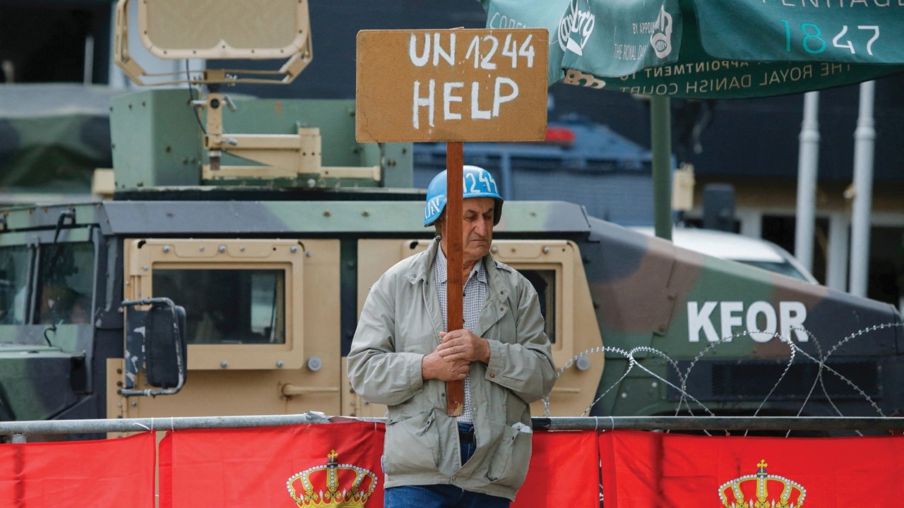 A person holds a placard as members of the NATO-led Kosovo Force (KFOR) stand guard outside ...