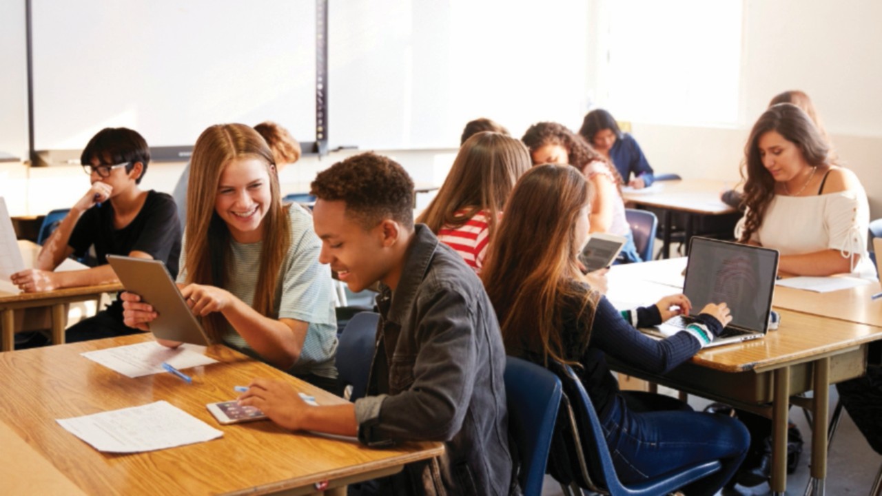 Wide Angle View Of High School Students Sitting At Desks In Classroom Using Laptops