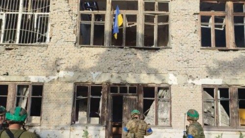 Ukrainian soldiers stand in front of a building with a Ukrainian flag on it, during an operation ...