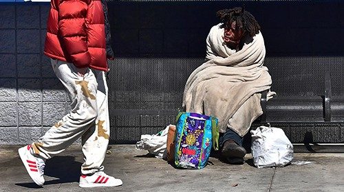 A pedestrian walks past a homeless on the streets of Los Angeles, California on February 24, 2022, ...