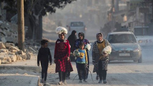 FILE PHOTO: A girl carries a stack of bread on her head as she walks with other people near rubble ...