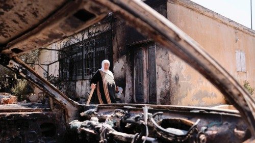 A Palestinian woman carries a piece of wood as she stands outside her house, which was set on fire ...