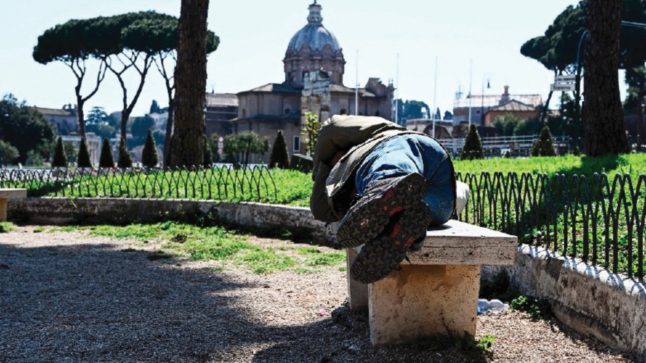 A homeless man sleeps on a public bench in Via dei Fori Imperiali in central Rome on March 19, 2020 ...