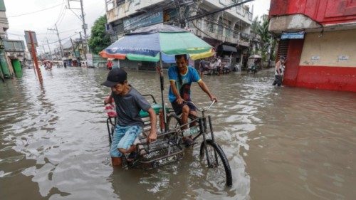 epa10770791 A man (L) alights from a tricycle along a flooded road in Valenzuela City, Metro Manila, ...