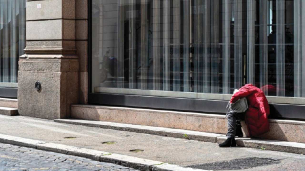 A homeless person sits by a shop on a deserted Via del Corso main shopping street on March 31, 2020 ...