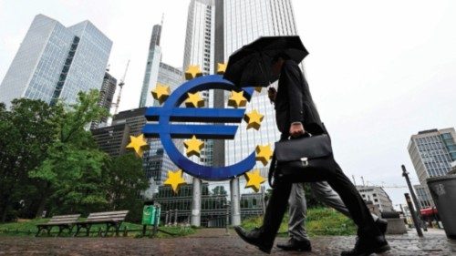 A man shelters from the rain under an umbrella as he walks past the Euro currency sign in front of ...