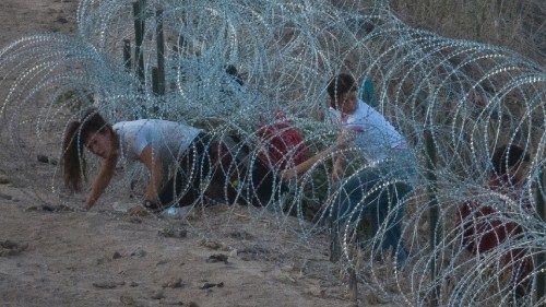 A woman from Colombia crawls through concertina wire, deployed to deter migrants, as she leads her ...