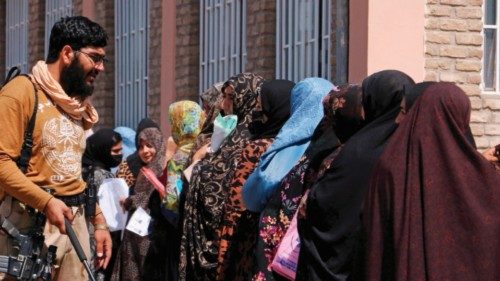 A Taliban security personnel gestures as women stand in a queue outside the passport office in Herat ...