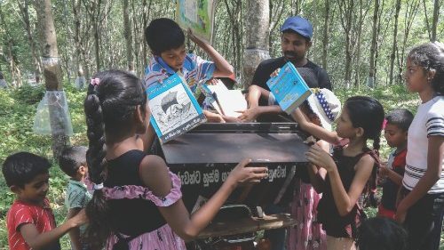 epa10824863 Mahinda Dasanayaka (C-R) distributes books for children from his mobile library ...
