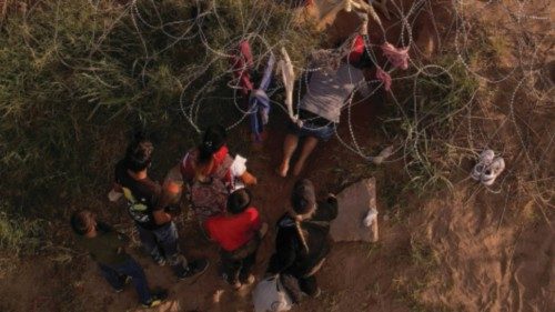 Migrants seeking asylum in the United States try to cross a wire fence deployed to inhibit the ...