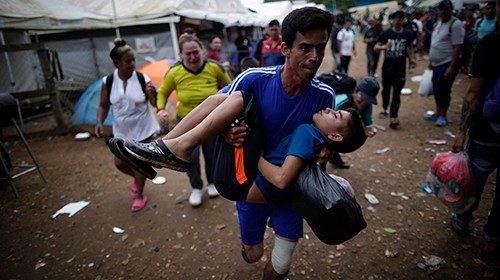 epa10875465 A man carries his fainted son while waiting in line for a bus transfer to Paso Canoas, ...