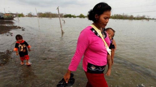 FILE PHOTO: A mother carries her baby as a child wades behind on a street flooded with sea water in ...