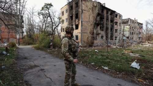 A Ukrainian serviceman stands next to residential buildings heavily damaged by permanent Russian ...