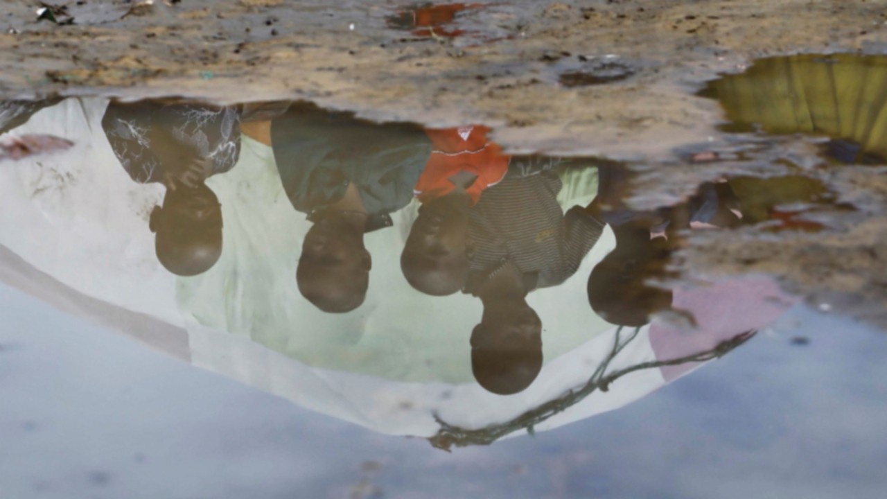 Children's reflections are seen in flood water outside their makeshift shelter at the Al-Hidaya camp ...