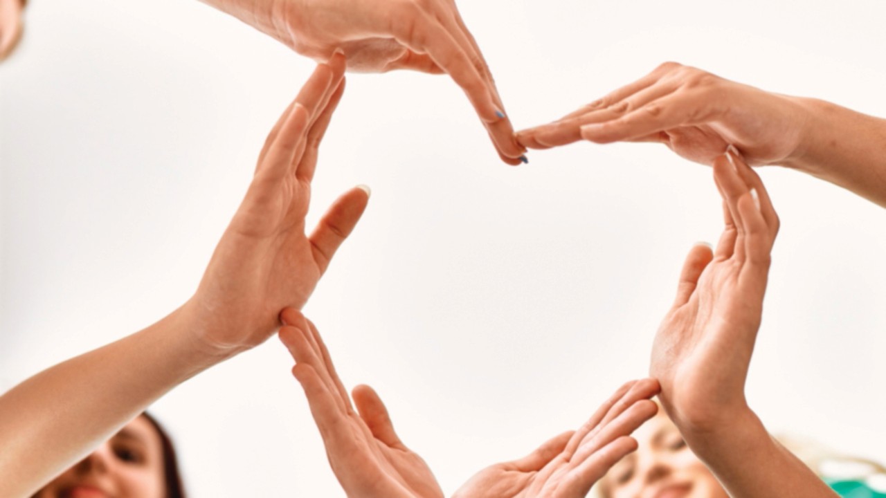 Group of young volunteers woman smiling happy make heart symbol with hands together at charity ...