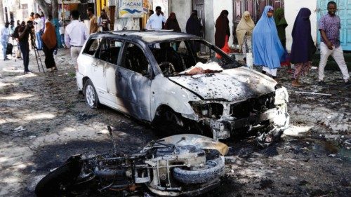 Somalis walk past the wreckage of a vehicle and a motorcycle destroyed at the scene of a suicide ...