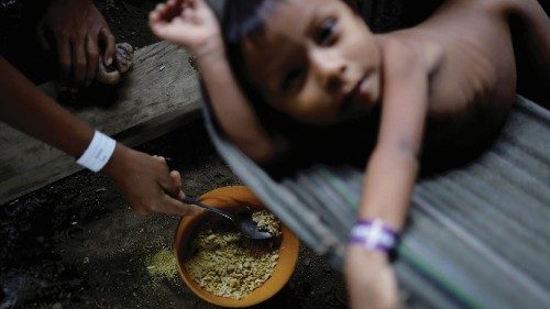 A Yanomami child is fed a mix of rice and farofa by his mother while receiving healthcare in the ...
