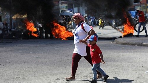 A woman and a child walk drive through a burning barricade, one of many across several ...