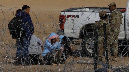 Migrants sit in El Paso, Texas, near a razor wire fence used to prevent them from crossing into the ...