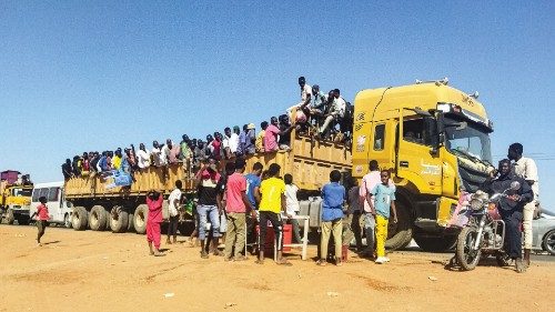 People displaced by the conflict in Sudan get on top of the back of a truck moving along a road in ...