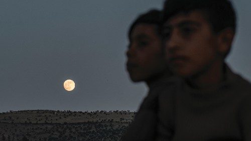 Children ride a donkey as the waxing gibbous moon rises in the countryside of the village of Tal ...