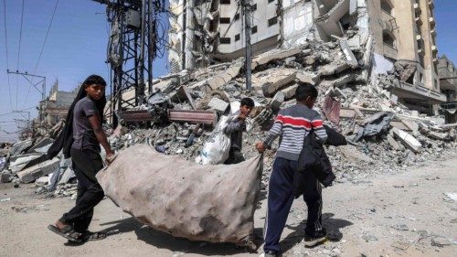 TOPSHOT - Boys walk with a large sack containing collected plastic past the rubble of a destroyed ...