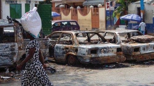 epa11266127 Pedestrian walk past the remains of burned vehicles in downtown Port au Prince, Haiti, ...