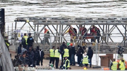 People, believed to be migrants, including one being carried on a stretcher, wait on the quayside to ... People, believed to be migrants, including one being carried on a stretcher, wait on the quayside to ...