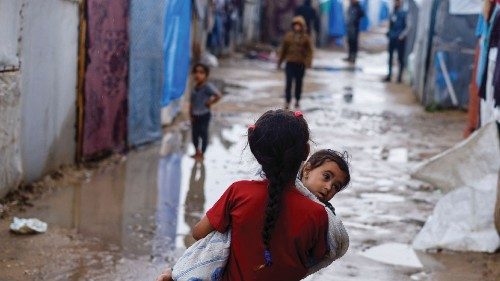 A displaced Palestinian girl holds a child as she walks at a tent camp on a rainy day, amid the ...