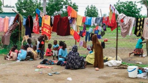 Families sit beneath clotheslines as they await meals provided through a charity initiative at a ... Families sit beneath clotheslines as they await meals provided through a charity initiative at a ...