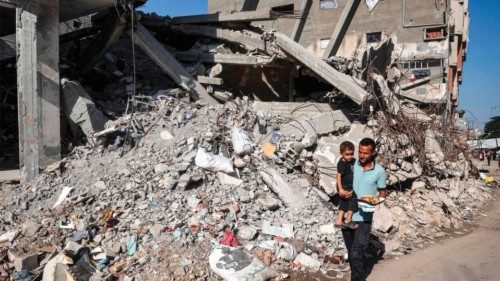 TOPSHOT - A man carries a child while walking past a collapsed building in the Bureij camp for ... TOPSHOT - A man carries a child while walking past a collapsed building in the Bureij camp for ...