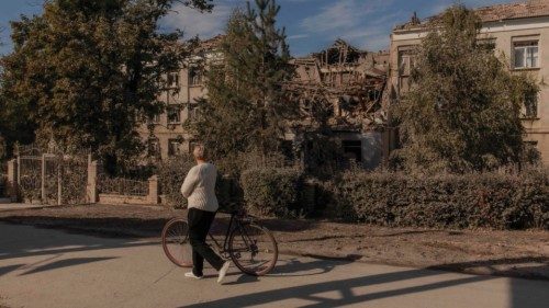 A woman cyclist walks with a bicycle next to a building damaged after an early morning Russian ... A woman cyclist walks with a bicycle next to a building damaged after an early morning Russian ...