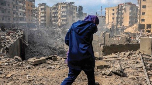TOPSHOT - A woman walks past a crater where a collapsed building stood following an overnight ... TOPSHOT - A woman walks past a crater where a collapsed building stood following an overnight ...