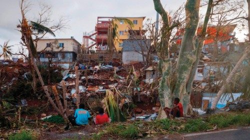 People sit next to their damaged houses in the city of Mamoudzou, on the French Indian Ocean ... People sit next to their damaged houses in the city of Mamoudzou, on the French Indian Ocean ...