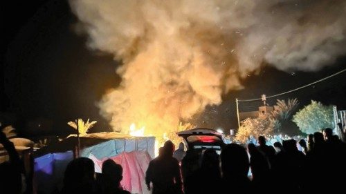 Smoke rises as people stand in a tent camp for displaced people, after an Israeli attack, according ... Smoke rises as people stand in a tent camp for displaced people, after an Israeli attack, according ...