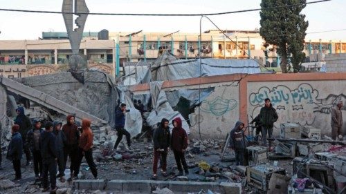 People stand next to the rubble of a school, housing displaced Palestinians, which was destroyed in ... People stand next to the rubble of a school, housing displaced Palestinians, which was destroyed in ...