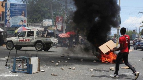 A man holds placards as he yells toward a patrol car near a burning barricade during a protest ... A man holds placards as he yells toward a patrol car near a burning barricade during a protest ...