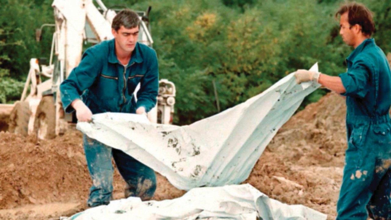 International War Crimes Criminal Tribunal investigators add a body bag to a pile of human remains ...