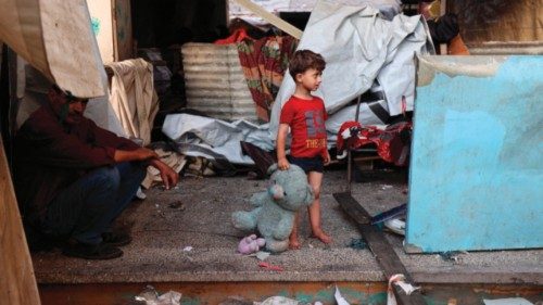 A Palestinian child holds a stuffed animal while standing at a school sheltering displaced ... A Palestinian child holds a stuffed animal while standing at a school sheltering displaced ...
