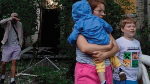 A woman with children walks past a damaged residential building following a Russian attack in Kyiv ...