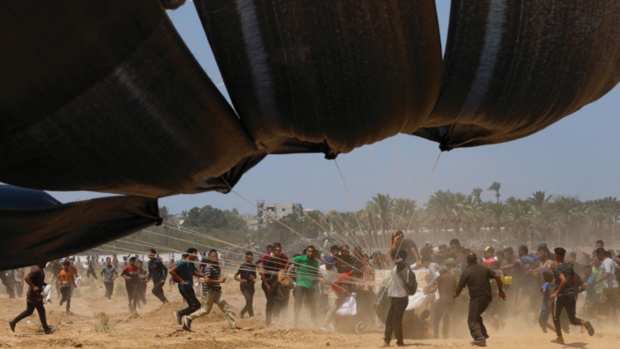 Palestinians run towards airdropped aid packages, in Deir Al-Balah, in the central Gaza Strip August ...