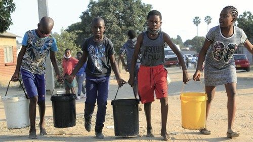 Crianças de Harare (Zimbábue), onde a população é atingida por uma grave seca, ajudam-se a carregar baldes de água (Epa)